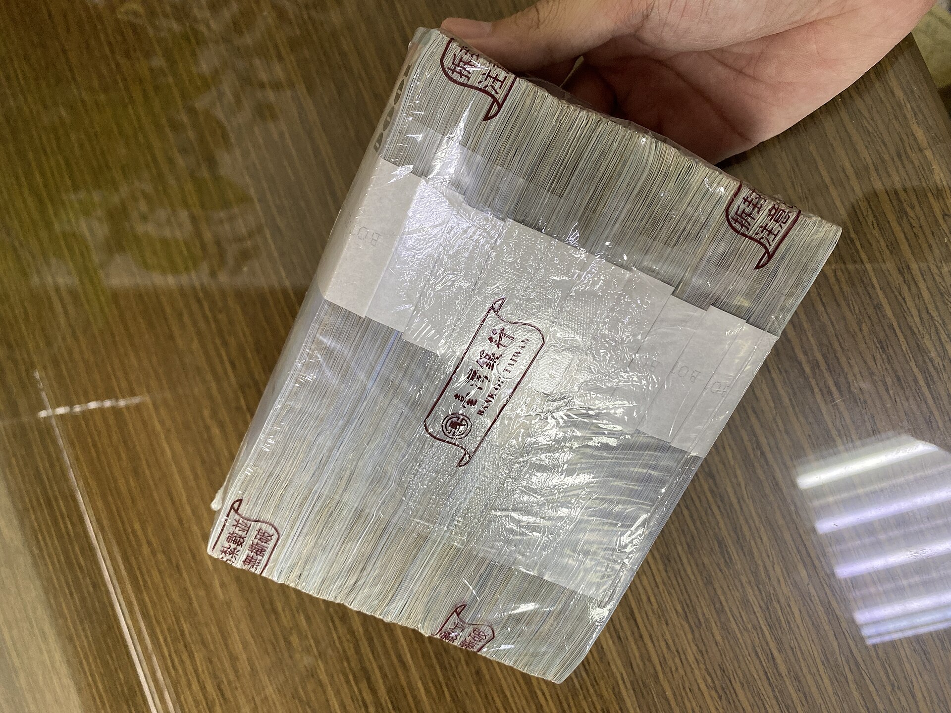銀行の帯封で束ねられた新台湾ドルの紙幣の束を手に持っている様子