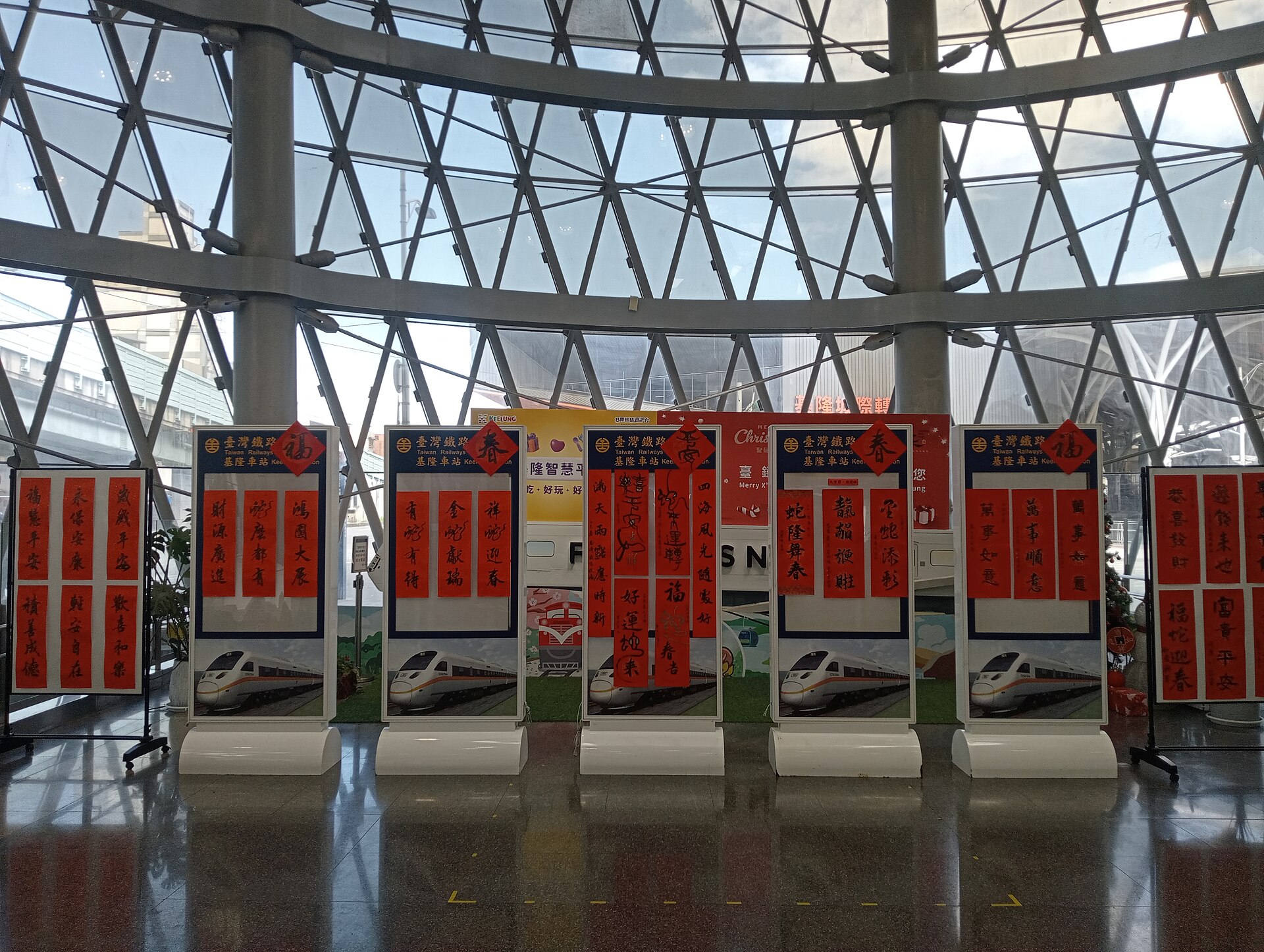 基隆駅の構内に並ぶ春聯（正月飾りの赤い対句）の展示、台湾鉄道の案内パネルとともに飾られている