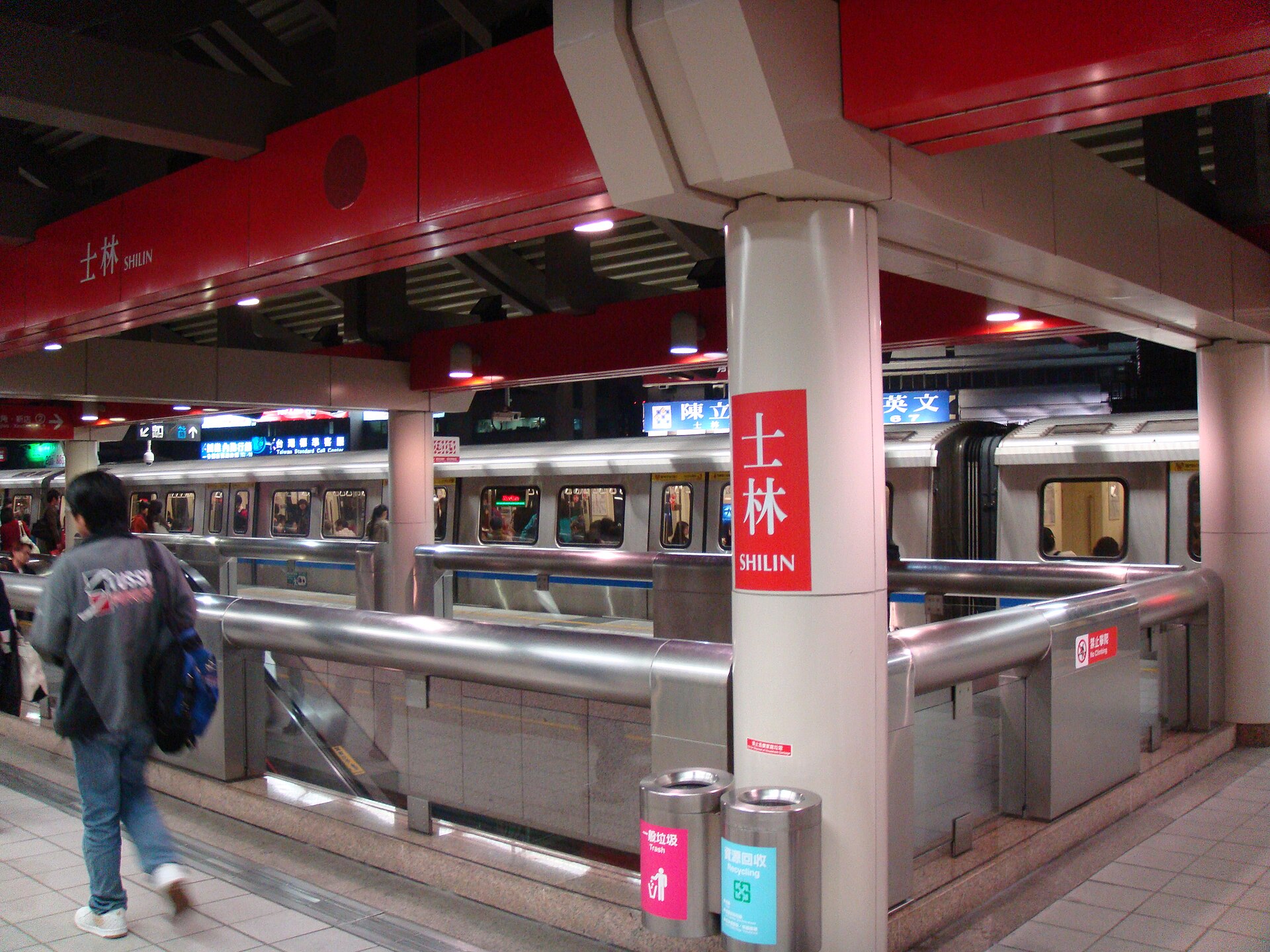 士林駅ホームの夜、明かりに照らされた線路と歩く乗客の後ろ姿