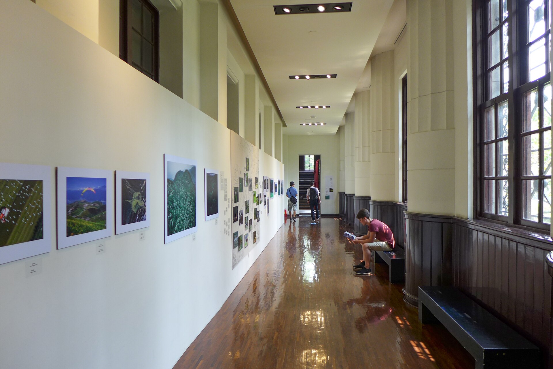 国立台湾博物館の長い回廊に並ぶ写真パネルと、ベンチに座る来館者