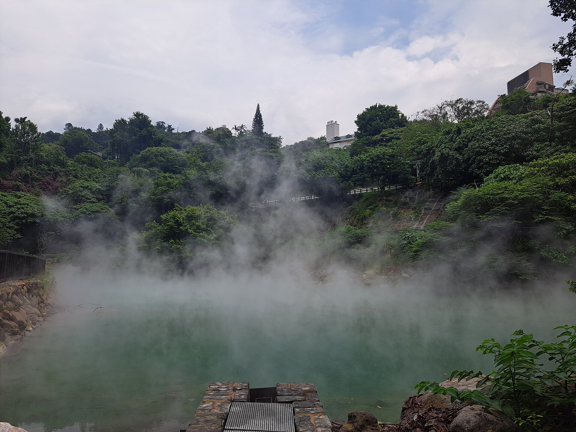 湯気に包まれた北投温泉「地熱谷」の乳白色の湯だまりと周囲の緑