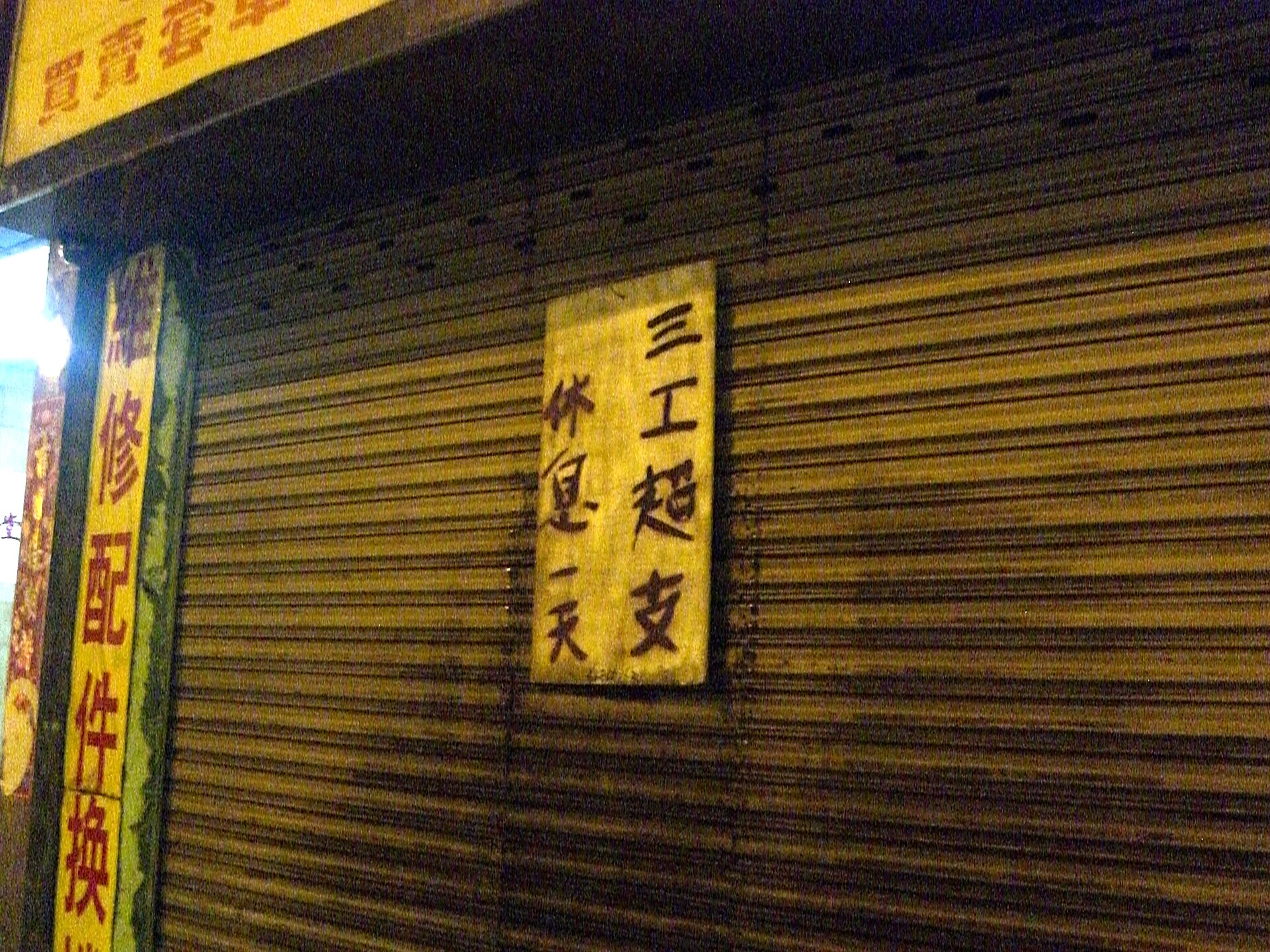 下ろされた金属製のシャッターに、休業を知らせる手書きの黄色い紙が貼られている様子