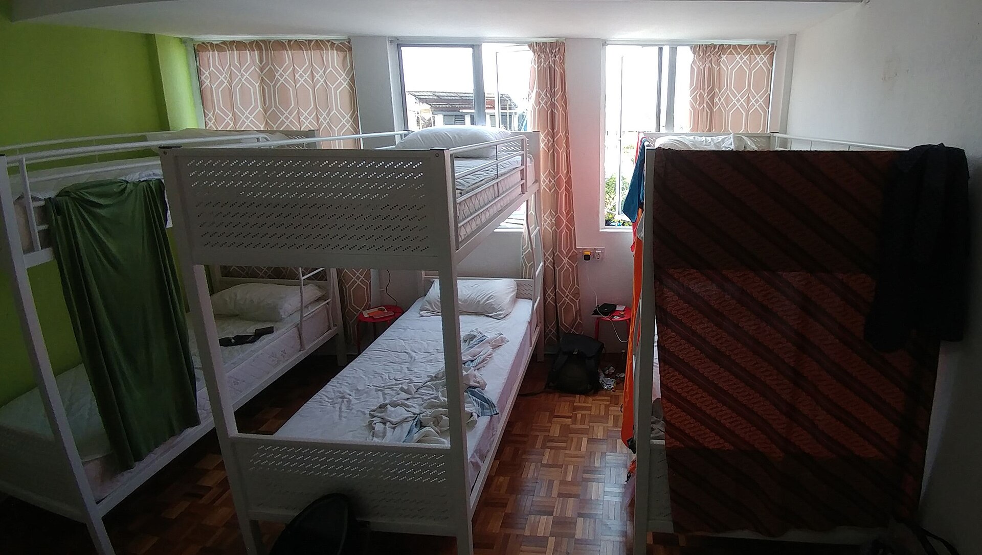 プライバシーカーテンで仕切られた二段ベッドが並ぶドミトリー部屋、宿泊者の荷物が置かれた室内