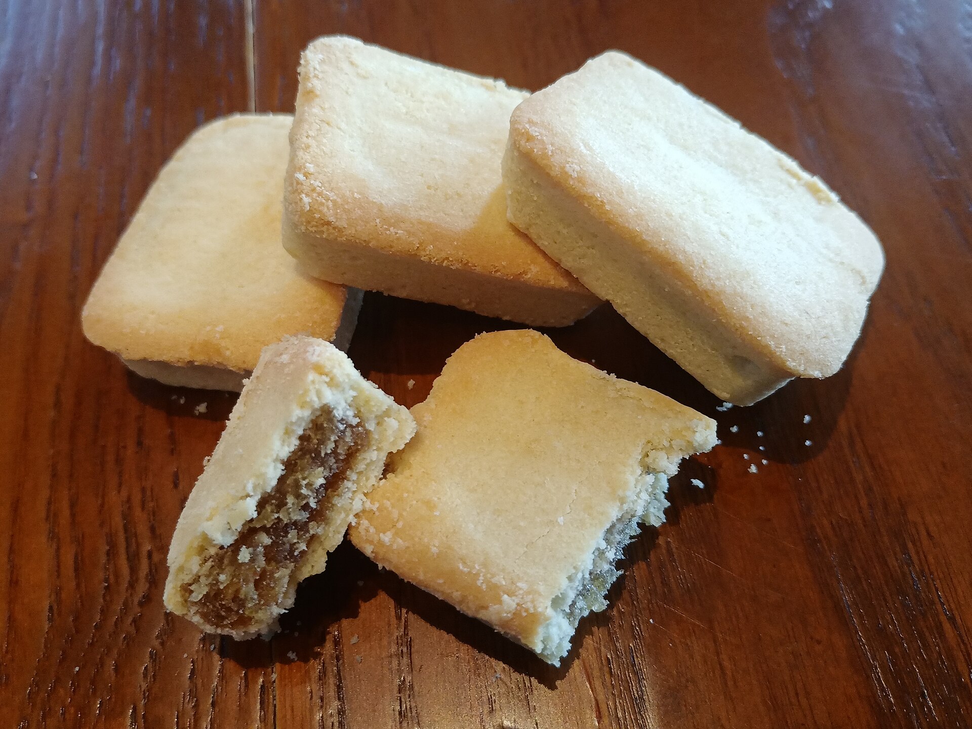 木目のテーブルに置かれた台湾式パイナップルケーキ数個、手前の一つは割られて中の餡が見えている