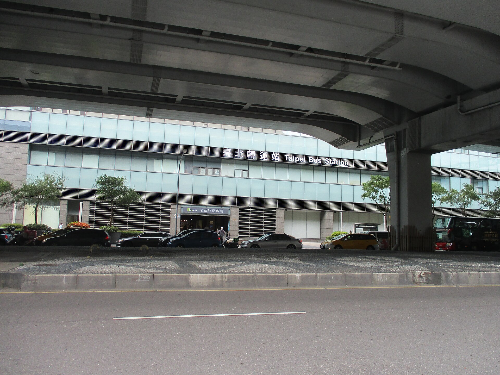 台北轉運站「臺北轉運站 Taipei Bus Station」の看板が見える建物外観と乗用車、清潔な高架下の乗り場周辺