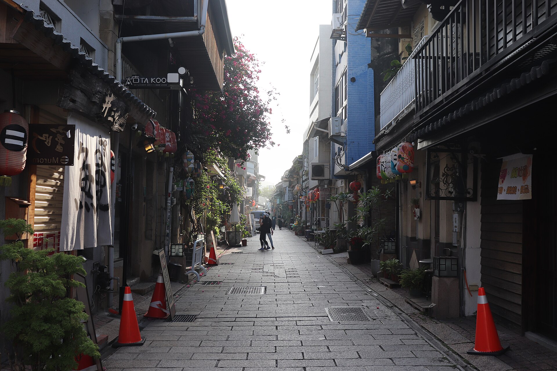 台南・神農街の朝、提灯が連なる老屋の並ぶ石畳の路地と観光客の後ろ姿