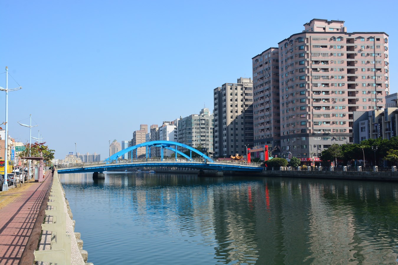 台南・安平の運河沿い、雲一つない青空の下に架かる青いアーチ橋と高層マンション群