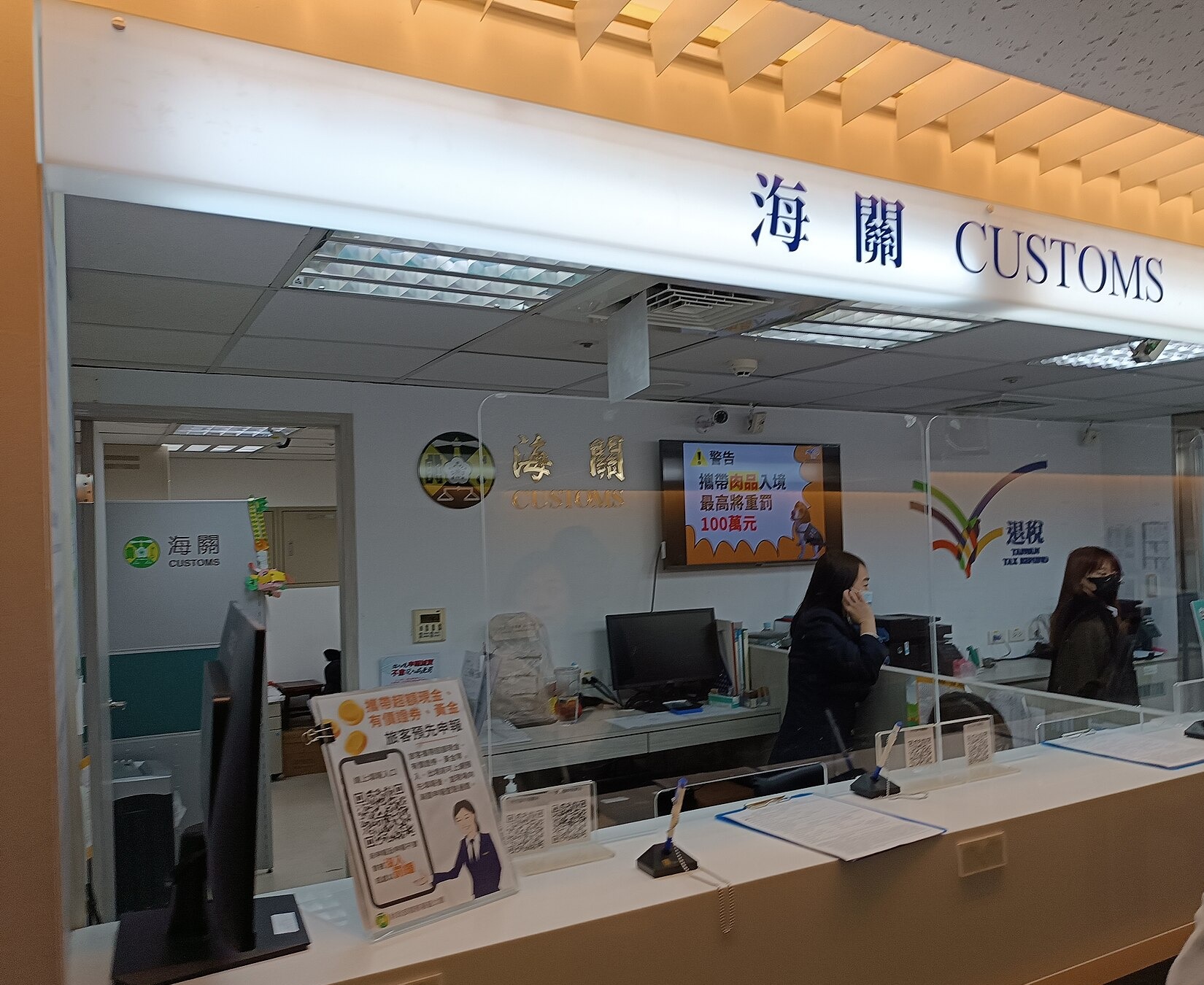 桃園国際機場第一ターミナルの海關（CUSTOMS）カウンター、背後の掲示モニターに「肉品を持ち込むと最高100万元の罰金」という警告が表示されている
