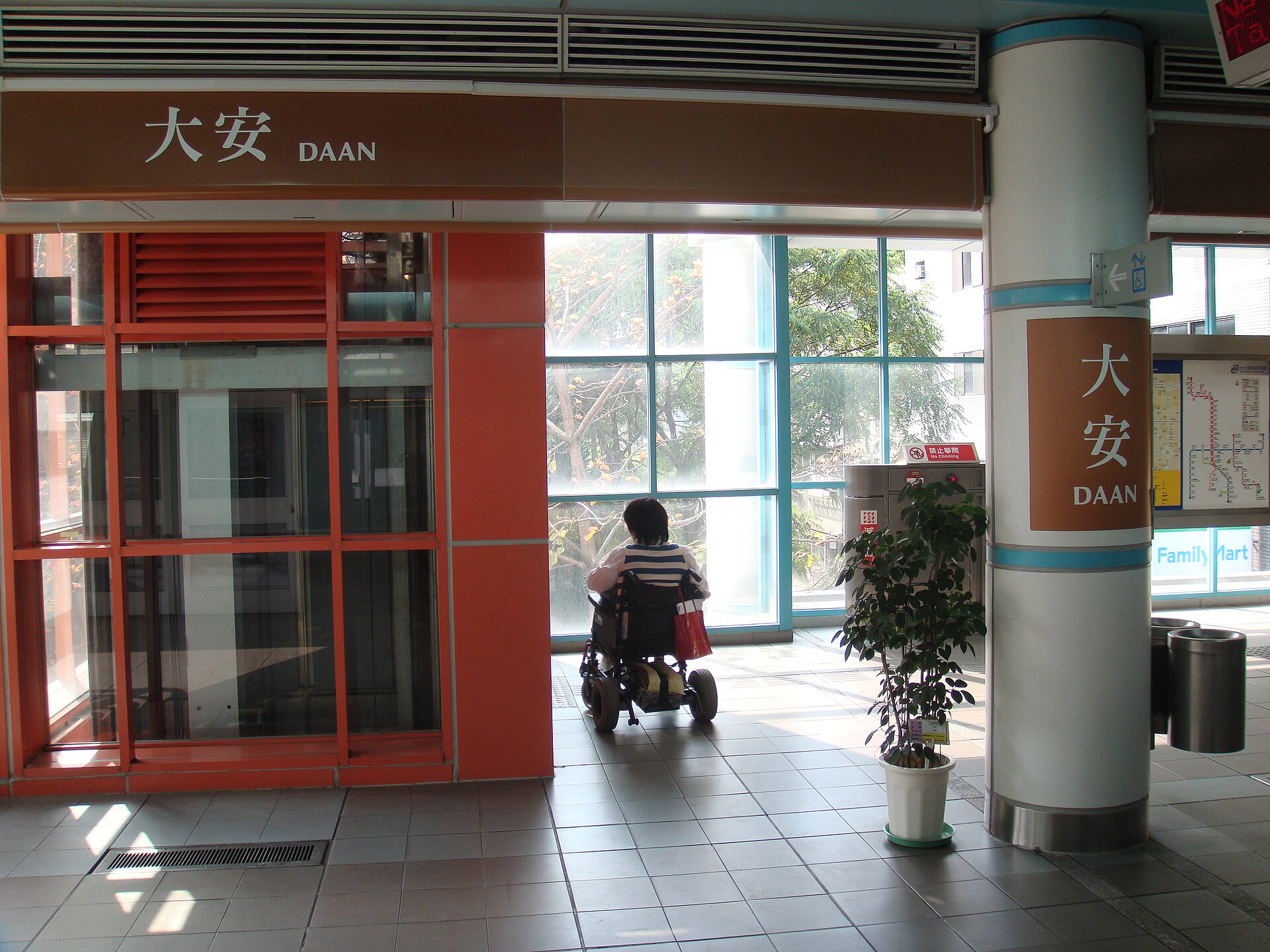 台北捷運大安駅の出入口そばで、電動車椅子に乗った人が後ろ向きでエレベーターのある方向を見ている
