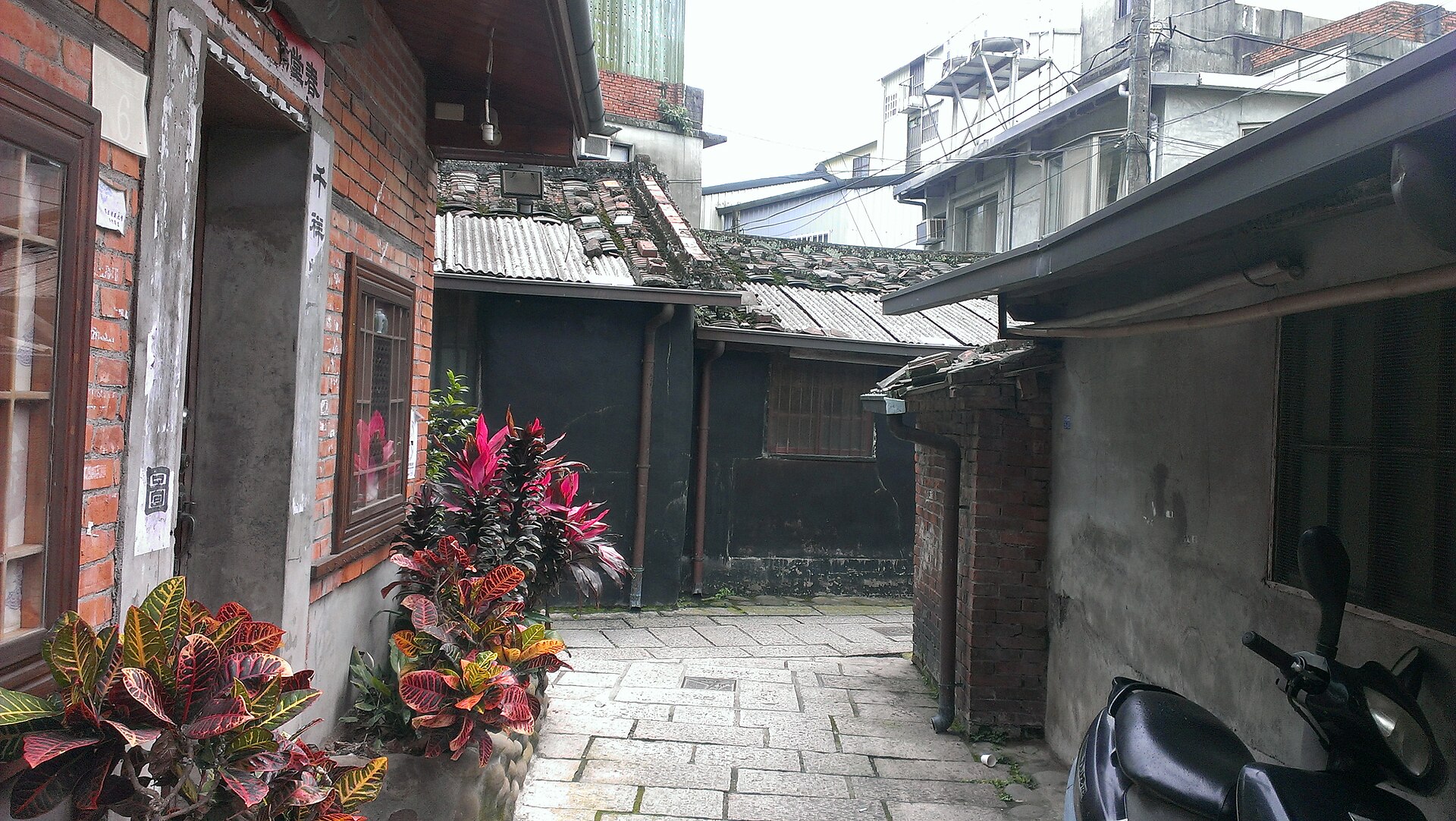 台湾の老街の路地にある赤レンガ造りの住宅の入り口、扉の脇に赤や黄色の葉をつけた鉢植えが並んでいる