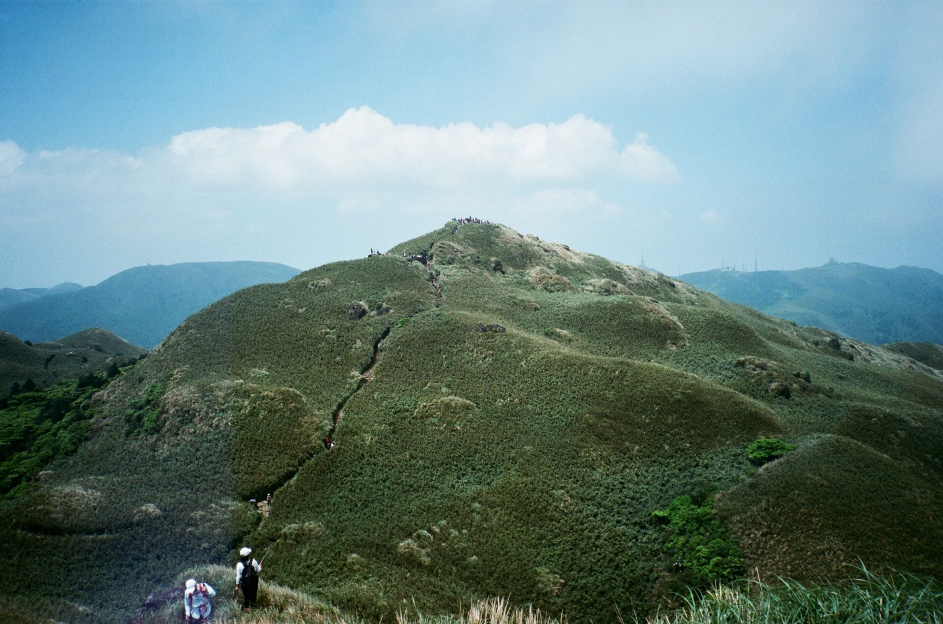 陽明山の稜線を歩く登山者たちの後ろ姿と青空に広がる草原