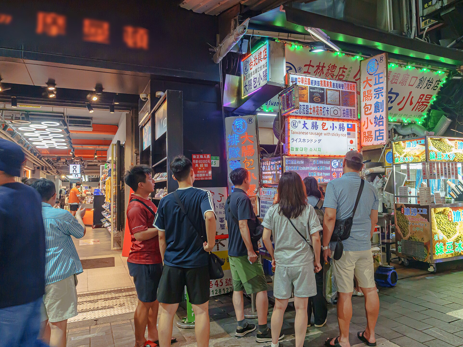 士林夜市の腸包小腸の店先に並ぶ観光客たち、ネオン看板が光る夜の様子